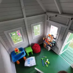 Jak urządzić domek dla dzieci w środku? Zabawki, stolik wodny, kuchnia i pufy tworzą przytulną przestrzeń do zabawy.