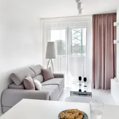 Przytulny, bardzo mały salon w bloku z szarą kanapą, stolikiem kawowym i widokiem na balkon.