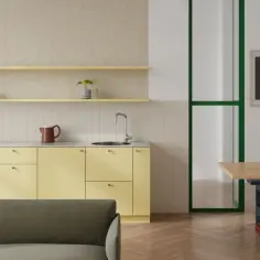 Jasna kuchnia w stylu modernistycznym z żółtymi szafkami, zieloną ramą drzwi i obrazami na ścianie.