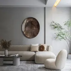 Nowoczesny salon w stylu minimalistycznym. Beżowa sofa, okrągły stolik kawowy, fotel i roślina w donicy tworzą przytulną przestrzeń.