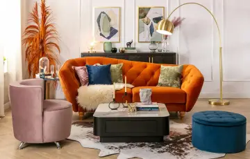 Salon w stylu francuskim: pomarańczowa kanapa, różowy fotel, złota lampa, dywan i dekoracje tworzą przytulną atmosferę.